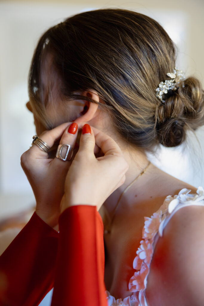 Detail shot of bridesmaid putting an earring in for the bride.