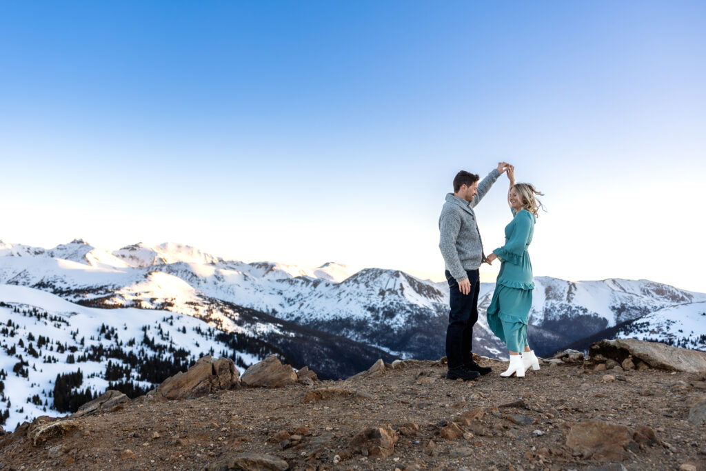 Couple dances on snowy mountaintop at sunrise during Colorado mountain elopement.